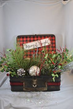 a suitcase filled with christmas decorations and greenery on top of a white cloth covered table