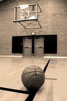 a basketball is sitting on the floor in front of an empty gym with two doors