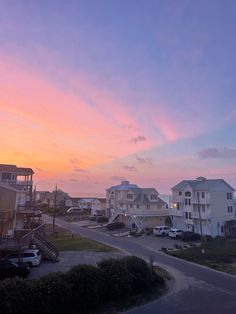 the sun is setting over some houses on the ocean side in front of an orange and pink sky