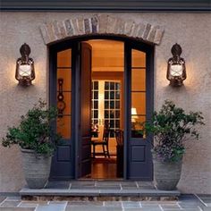 the front entrance to a house with potted plants and two lights on each side