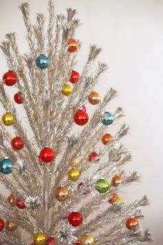 a white christmas tree with multi colored ornaments on it's top and silver branches