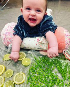 a baby sitting on top of a table surrounded by lemons and peas