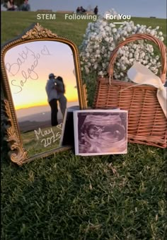 a couple's wedding pictures are placed in front of a basket and mirror on the grass