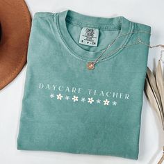 a t - shirt that says day care teacher with daisies on it and a hat next to it