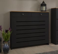 a black dresser with two drawers and a vase on the floor in front of it