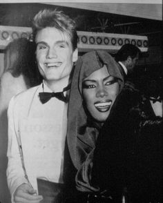 a man standing next to a woman in a tuxedo and wearing a head scarf