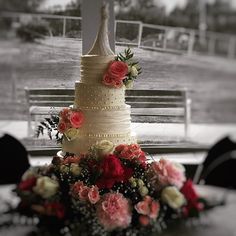 a wedding cake sitting on top of a table next to a park bench with red and white flowers