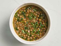 a bowl filled with beans and greens on top of a white countertop next to a spoon