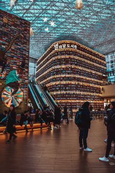 people are standing in the middle of a large building with an escalator and bookshelves