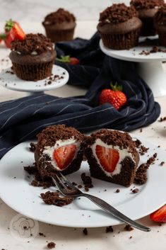 chocolate cupcakes with strawberries and whipped cream are on white plates next to each other