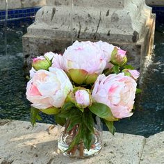 a vase filled with pink flowers sitting on top of a stone wall next to a pool