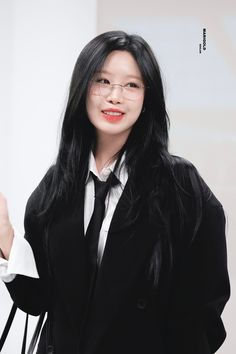 a woman with long black hair and glasses is holding a white paper in her hand