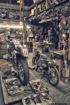 two motorcycles are parked in a garage with tools on the floor and other items around them