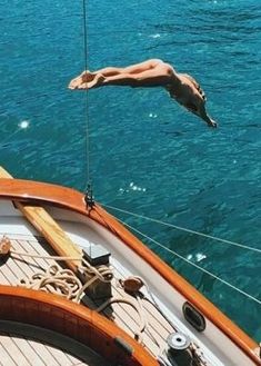 a man is jumping off the side of a boat into the water while another person swims in the background