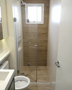 a white toilet sitting next to a shower in a bathroom under a window on top of a wooden floor