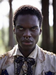 a man with an unusual nose ring wearing a shirt and tie in front of trees