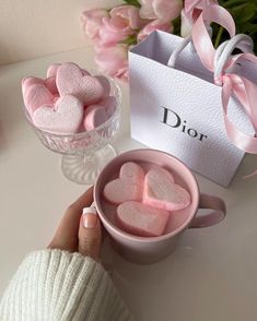 a pink heart shaped marshmallows in a cup next to a bouquet of flowers