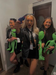 two women and one man are posing for a photo with green alien dolls in front of them