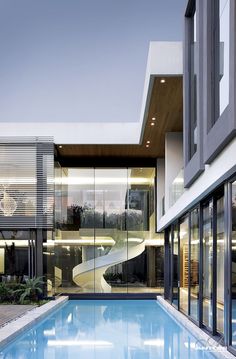 an empty swimming pool in front of a modern house with glass walls and stairs leading up to the upper floor