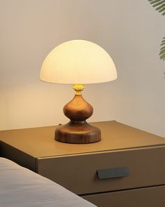 a lamp is sitting on top of a nightstand next to a plant and a bed