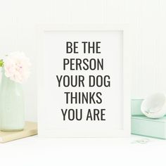 a white framed print with the words be the person your dog thinks you are next to a green vase