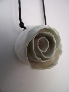 a white rose is hanging from a black cord on a wall with a knot around it