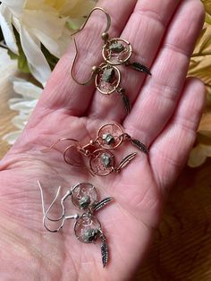 three pairs of earrings sitting in the palm of someone's hand next to flowers