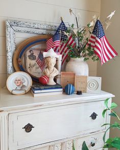 a white dresser topped with american flags and other items on top of it next to a potted plant