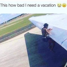 a man sitting on the wing of an airplane looking at his cell phone and texting,'this how bad i need a vacation? '