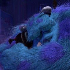 a blue furry animal sleeping on top of a purple bed next to a stuffed mouse