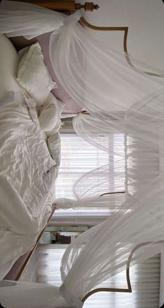 the bed is made up with white sheets and draps on top of it