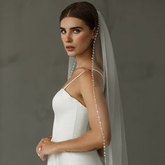 a woman wearing a white wedding veil with pearls on the side and her arms crossed