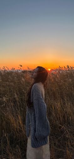 a woman standing in tall grass looking up at the sun