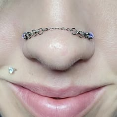 a woman's nose has a chain attached to her nose with two piercings on it