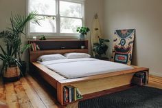 a bed sitting in the middle of a room next to a window with potted plants