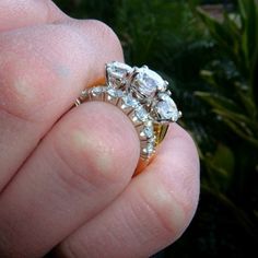 a hand holding a gold ring with three stones on it's side and the center stone is surrounded by smaller diamonds