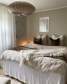 a bedroom with a large bed and white drapes on the windowsill, along with a round mirror hanging from the ceiling