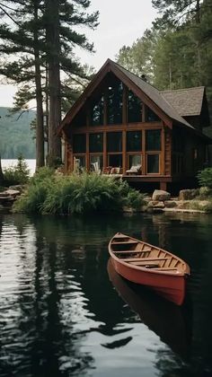 a small red boat sitting on top of a lake next to a wooden cabin with large windows