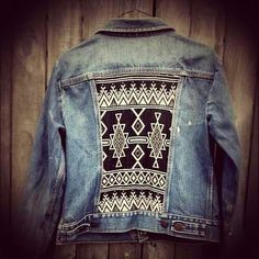 a denim jacket with an embroidered design on it hanging up against a wooden wall in front of a door