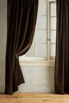 an open window with brown curtains in front of it and a wooden floor next to it