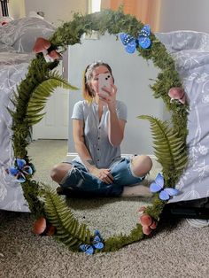 a woman sitting on the floor in front of a mirror with flowers and butterflies around it