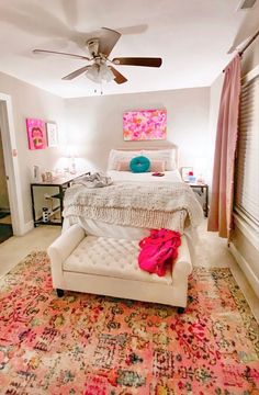 a white bed sitting next to a pink rug on top of a wooden floor under a ceiling fan