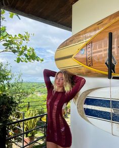 a woman standing next to a surfboard on the side of a building with trees in the background