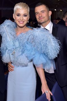 two people standing next to each other wearing blue dresses and feathered shawls at an event