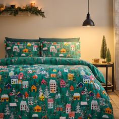 a bed covered in a green christmas themed comforter and pillow case with houses on it