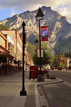 an empty street with mountains in the background and buildings on both sides that are lined with shops