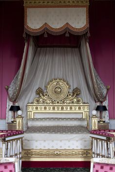 an elaborately decorated canopy bed in a pink and white room with gold trimmings