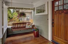 a porch with a wooden swing and potted flowers on the front door sill