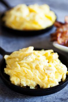 scrambled eggs in a skillet with bacon on the side