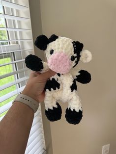 a hand holding a small black and white cow stuffed animal in front of a window